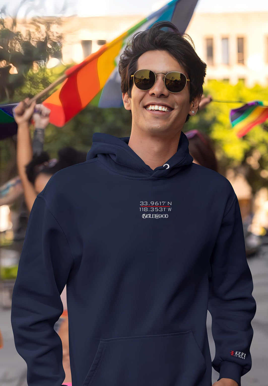 A man wearing a navy blue hoodie stands tall as a captivating rainbow flag waves behind him.