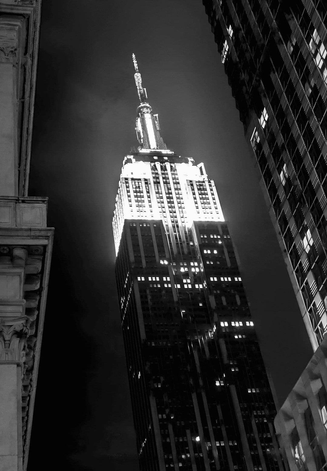 A black and white photograph of the Empire State Building, a classic structure contrasting with the lively metropolitan backdrop, depicts the building's enduring grace.