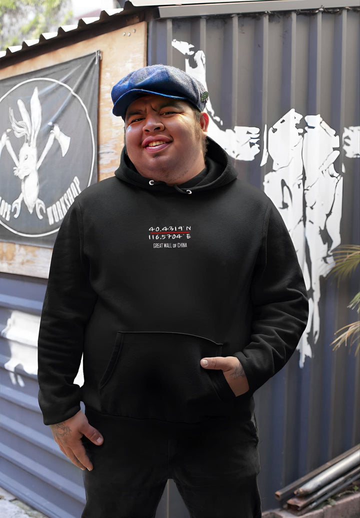 A smiling man standing in front of a building wearing a black Great Wall of China coordinates  hoodie.