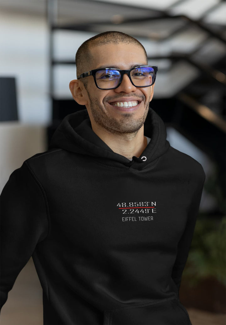 On a staircase, a bearded man wearing a black hoodie logo smiles and strikes a pose.