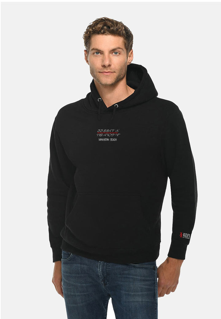 A man standing and wearing a Manhattan Beach, California GPS coordinates black hoodie.