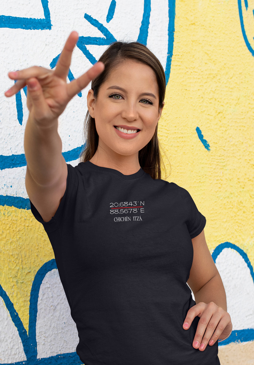 A woman in a black logo t-shirt extends the peace sign before a wall, creating a visual symphony of positivity and self-empowerment.
