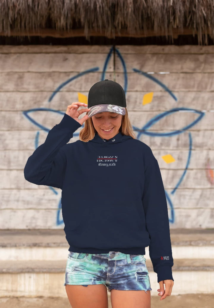 At the beach, there is a girl wearing a blue hoodie and a cap.