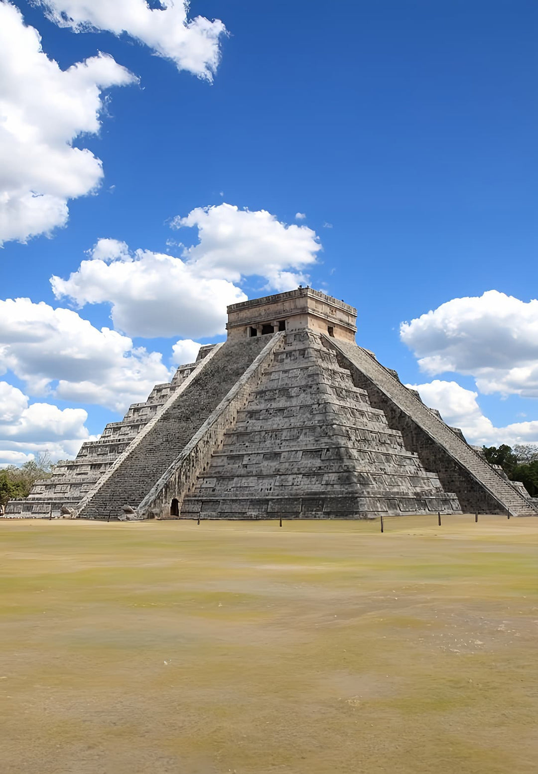 Chichen Itza's massive pyramid stands out against a blue sky in the middle of a green field.