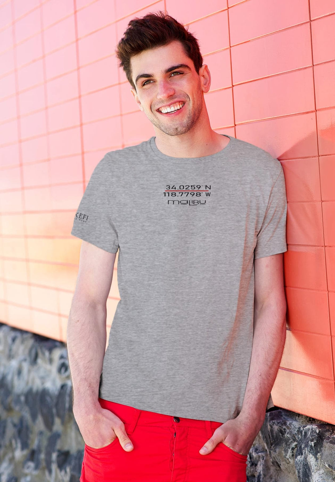 With a gentle smile, he leans on the wall in his gray tee, embodying a moment of serene happiness.