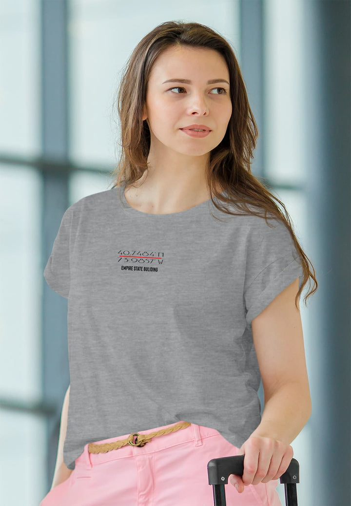 A woman reflecting effortless chic carries a rolling suitcase while wearing a gray t-shirt. 