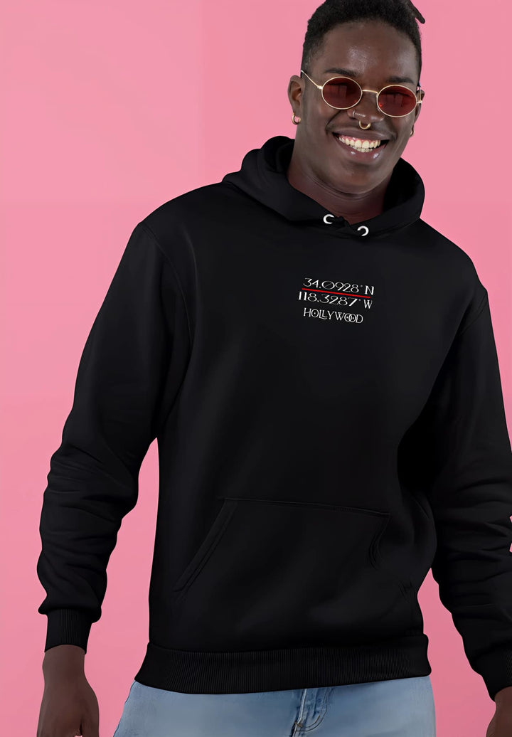 A smiling male figure, wearing a black hoodie and sunglasses, while in Hollywood, California.