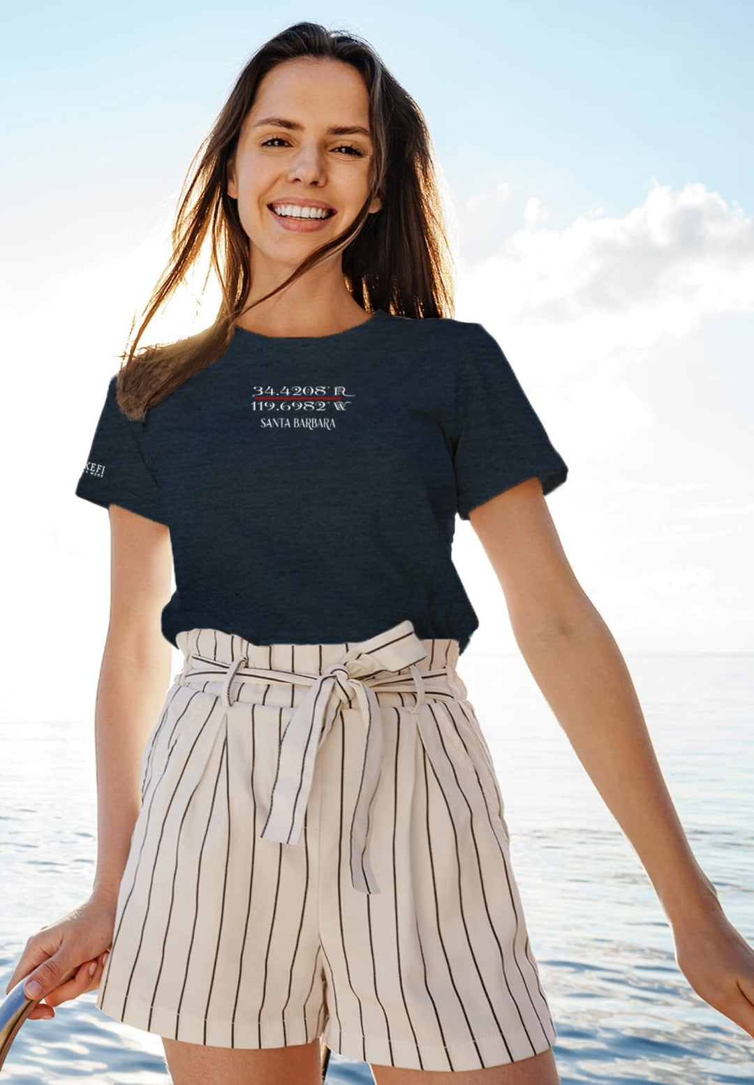 With the wind in her hair and the horizon before her, she stands on a boat, a vision in a serene blue t-shirt.