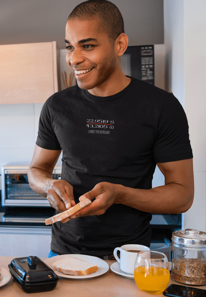 In the morning light, a man adorned in a black Christ the Redeemer t-shirt anticipates the first bite of breakfast, a moment embraced.