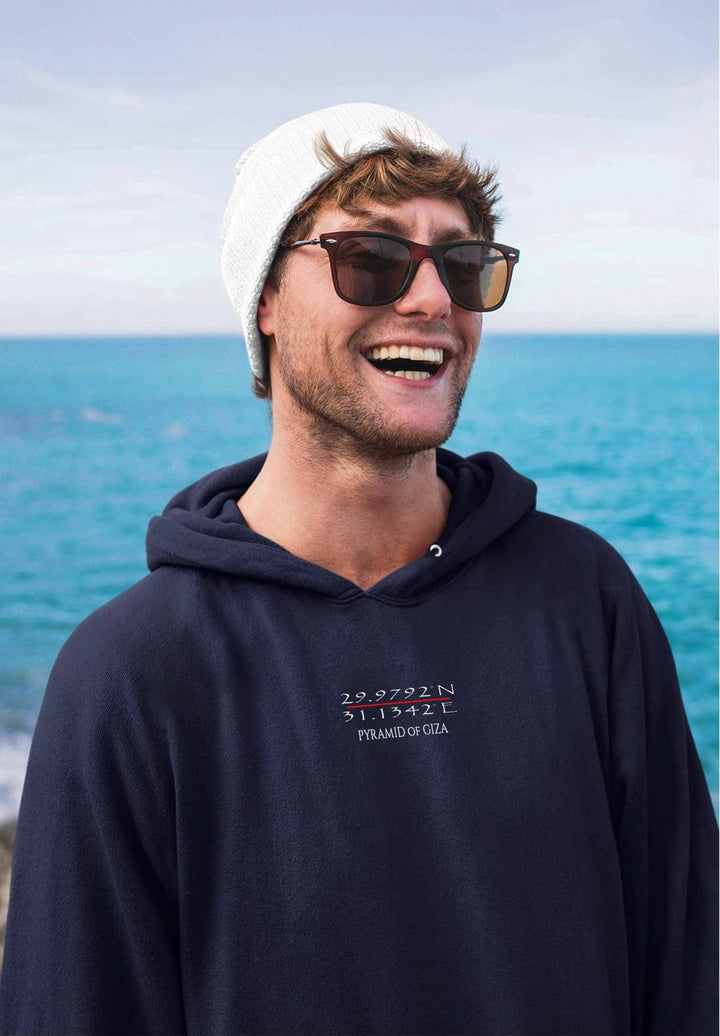 A fashion-forward moment unfolds as the man effortlessly pairs his blue hoodie with a snug beanie, showcasing his distinctive style by the sea.