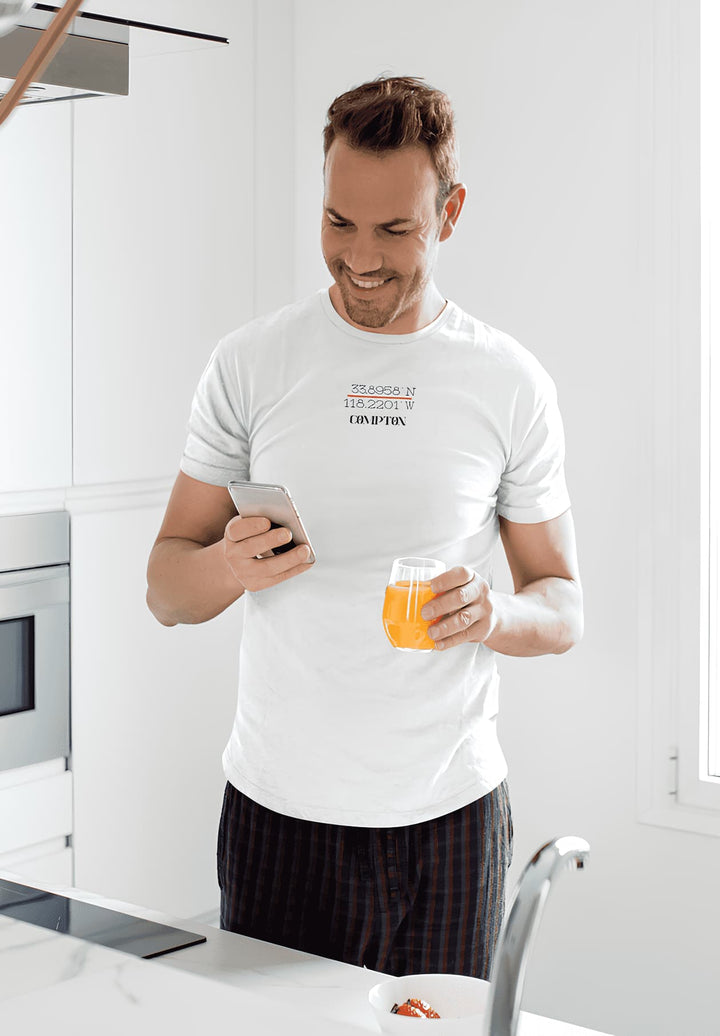 In the soft morning light, a man savors orange juice, his heart wrapped in the warmth of a Compton tee.