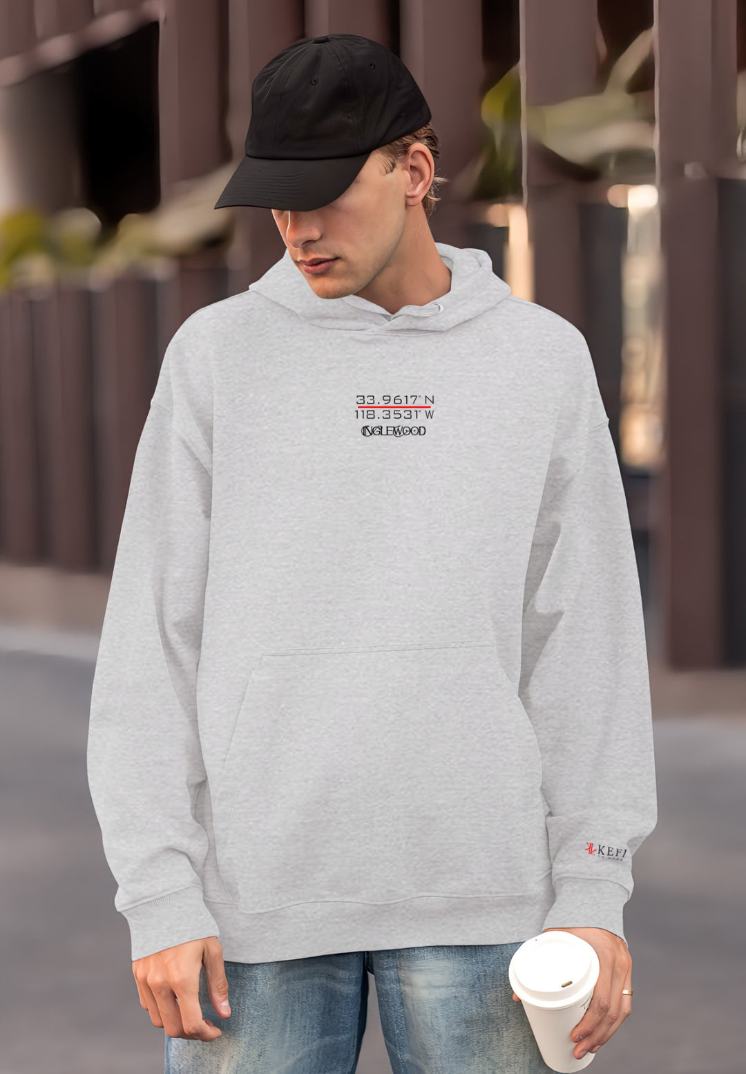 A gentleman standing wearing a gray hoodie can be seen holding a coffee cup in their hand. 
