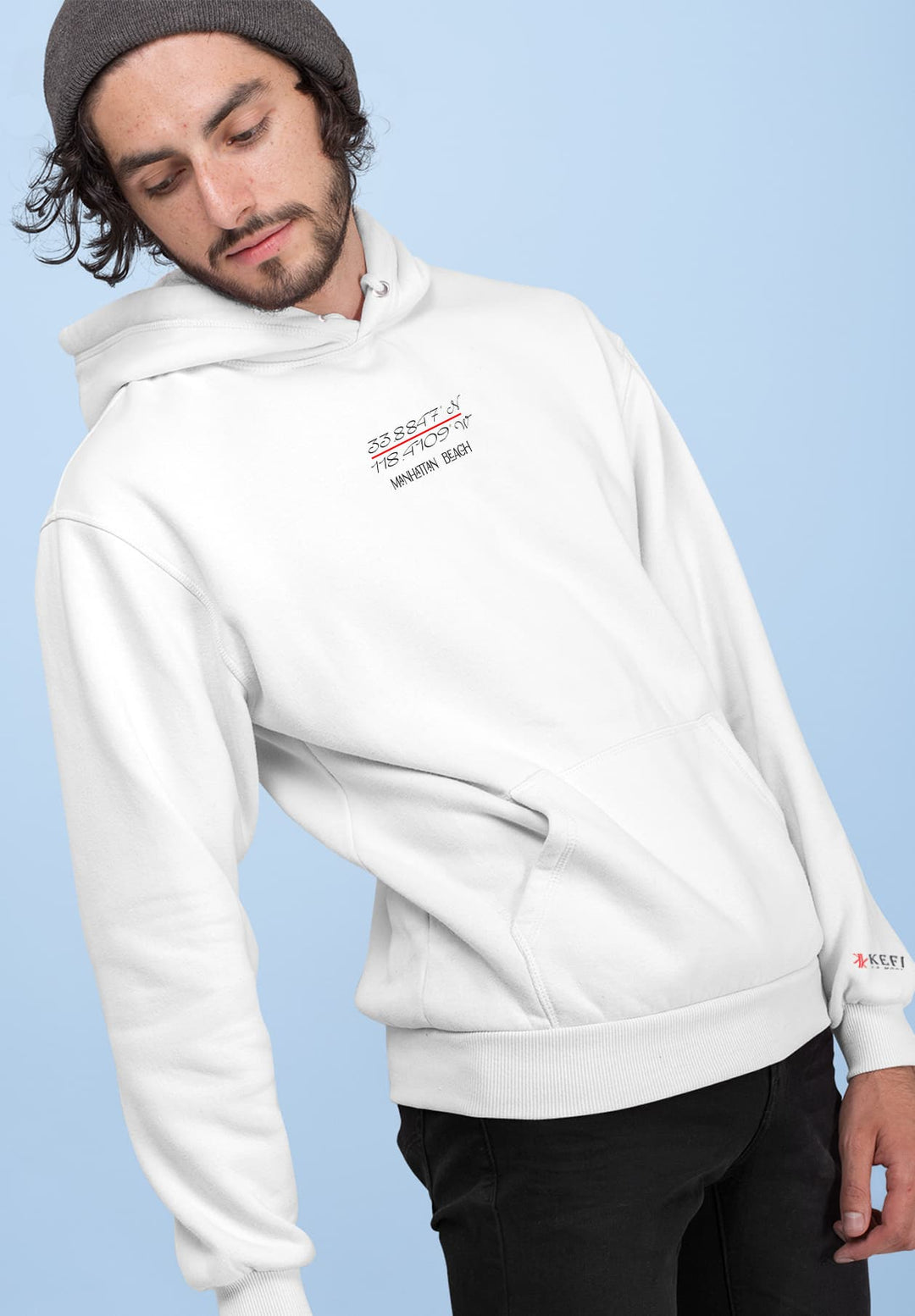 A man leaning and sporting a white Manhattan Beach hoodie logo and black pants.