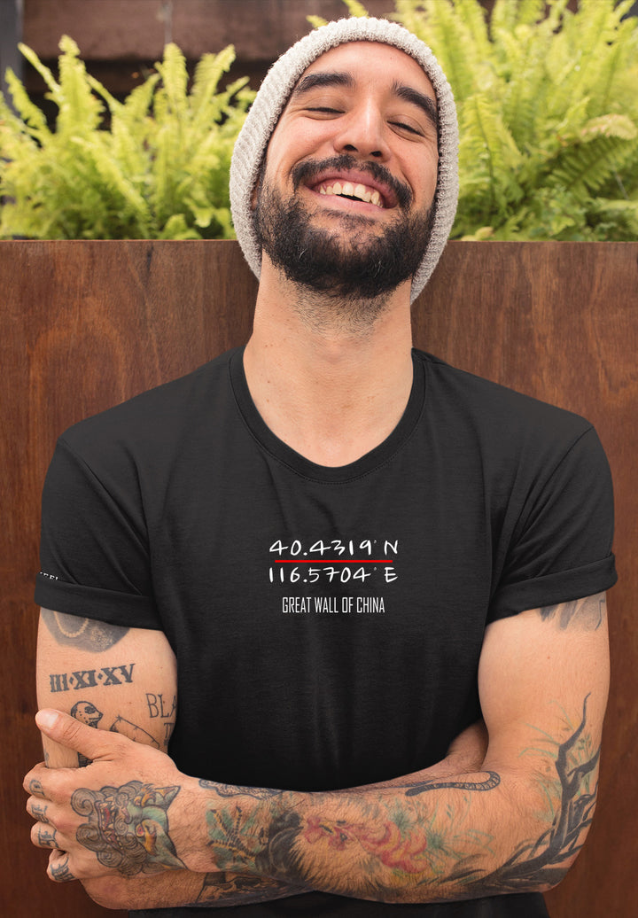 A beanie crowns the man in a black Great Wall tee, tattoos sharing stories, as his smile bridges worlds emotionally.