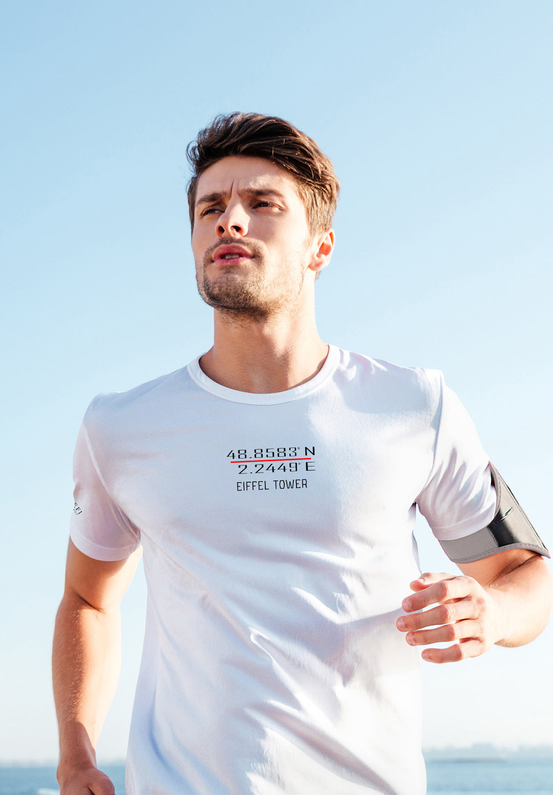 A man in a white Eiffel Tower tee sprints along the shore, chasing dreams and leaving footprints of passion behind.