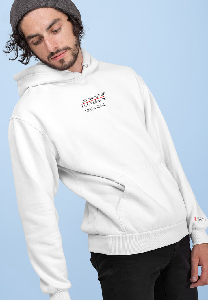 A man leaned against the wall while wearing a white hoodie and black pants.