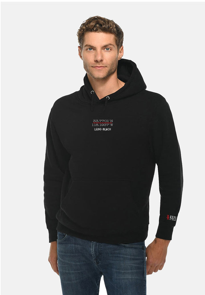 A man standing wearing a black hoodie with a red and white logo on it.