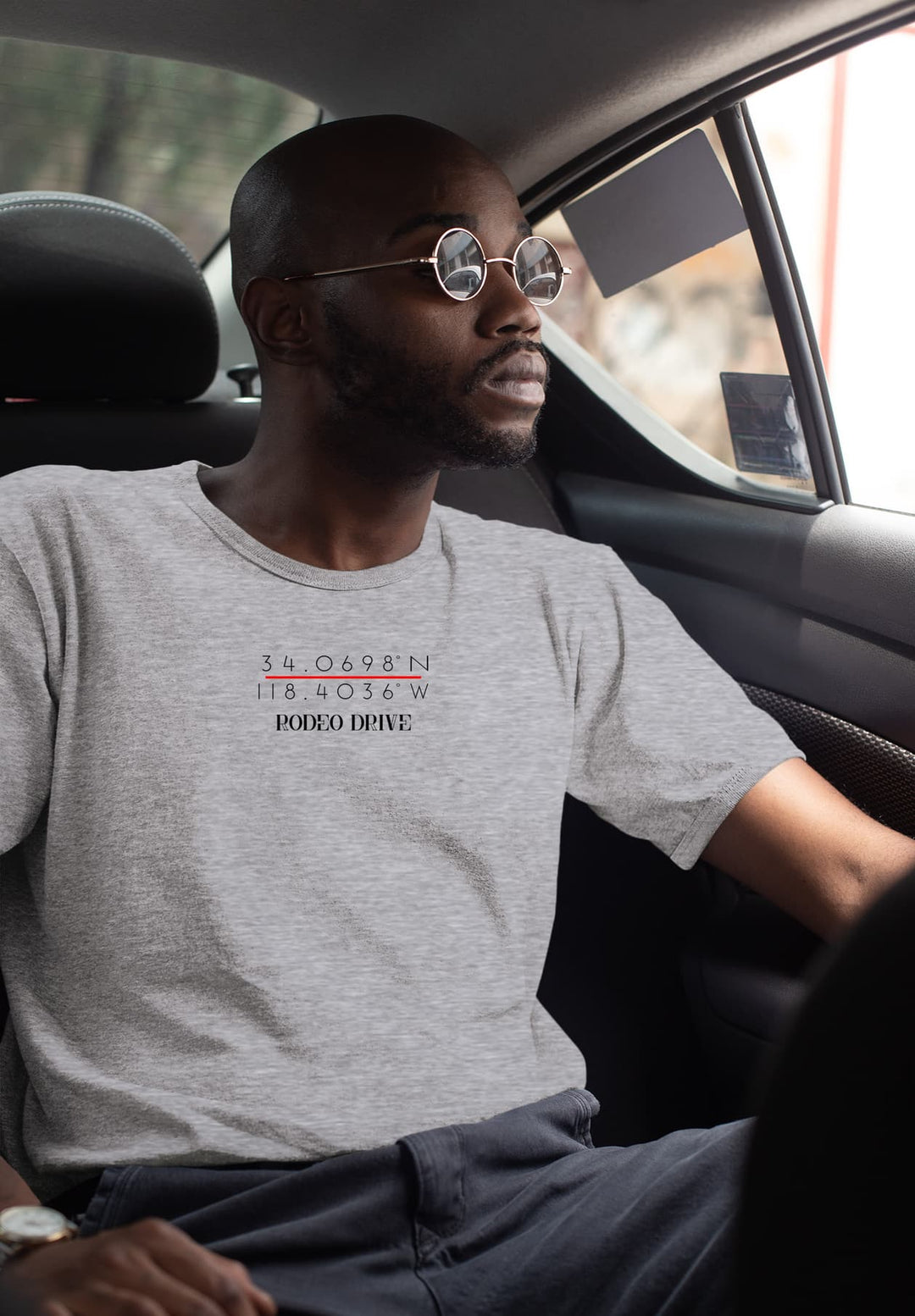 Enveloped in the backseat, memories flicker as he travels in his gray Rodeo Drive tee, each mile a reverie.