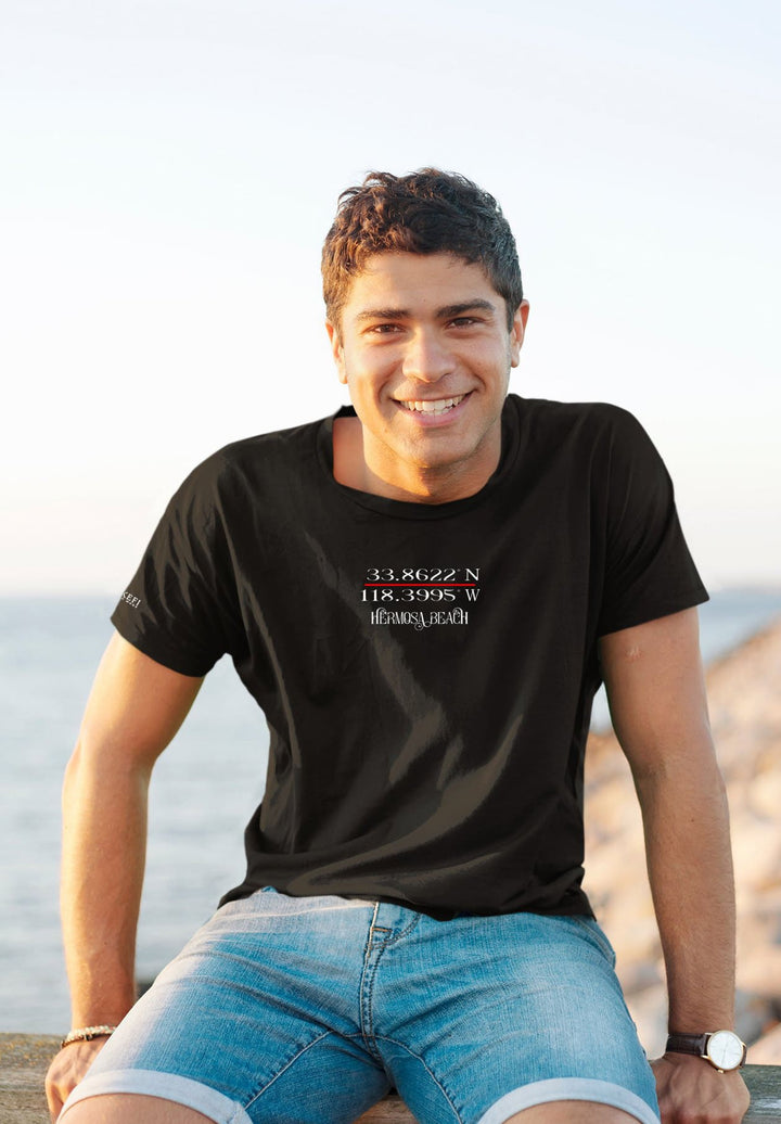 A black tee captures stories, the man seated by the ocean—a tapestry of emotions woven in the sea's reflection.