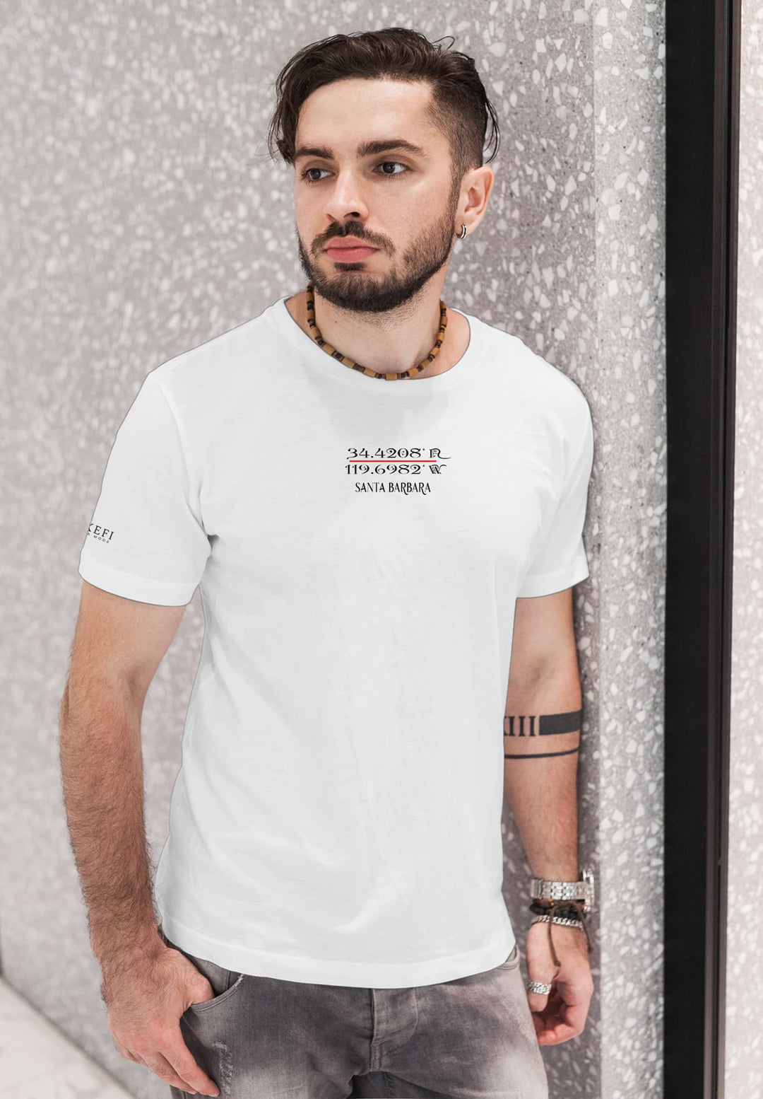 Standing by the wall, he wears a Santa Barbara white tee, moments of sunshine and a cherished snapshot.