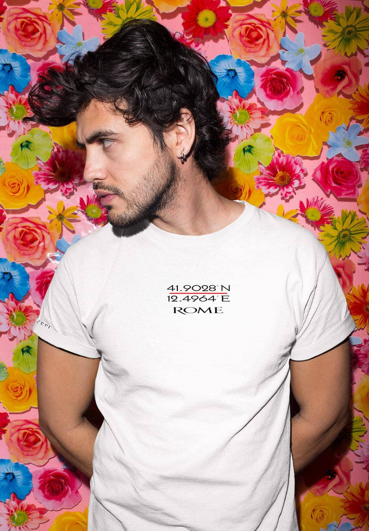 Against the flower wall, he stands, his white tee a canvas for moments of serenity and cherished memories.