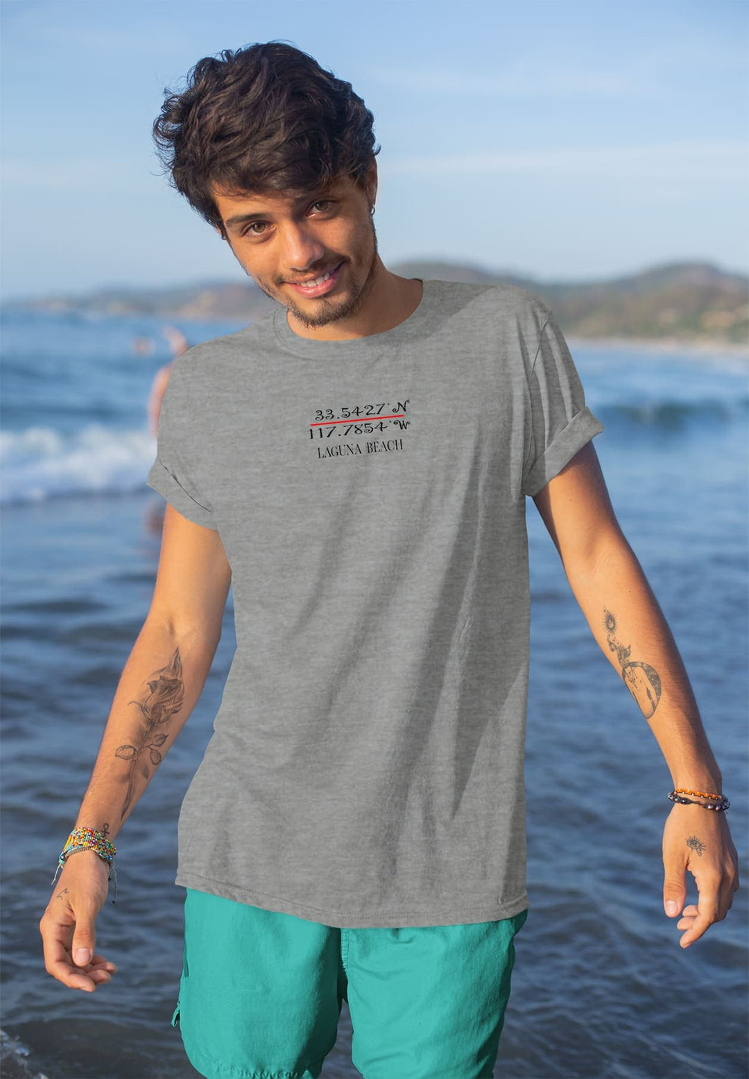 Standing in the water, gray tee clinging, he smiles—a moment etched in seaside joy, where waves echo laughter.
