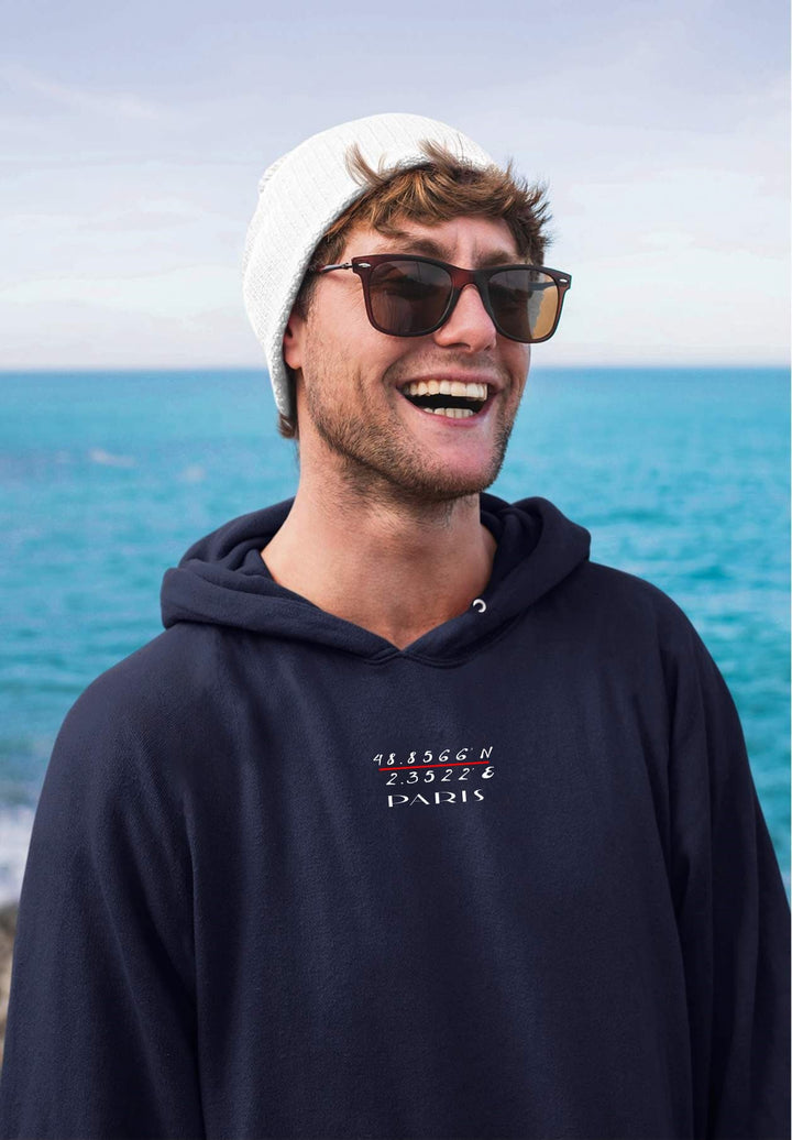 With his captivating smile, the man makes a fashion statement in a trendy Paris blue hoodie, perfectly complementing the oceanic scenery.