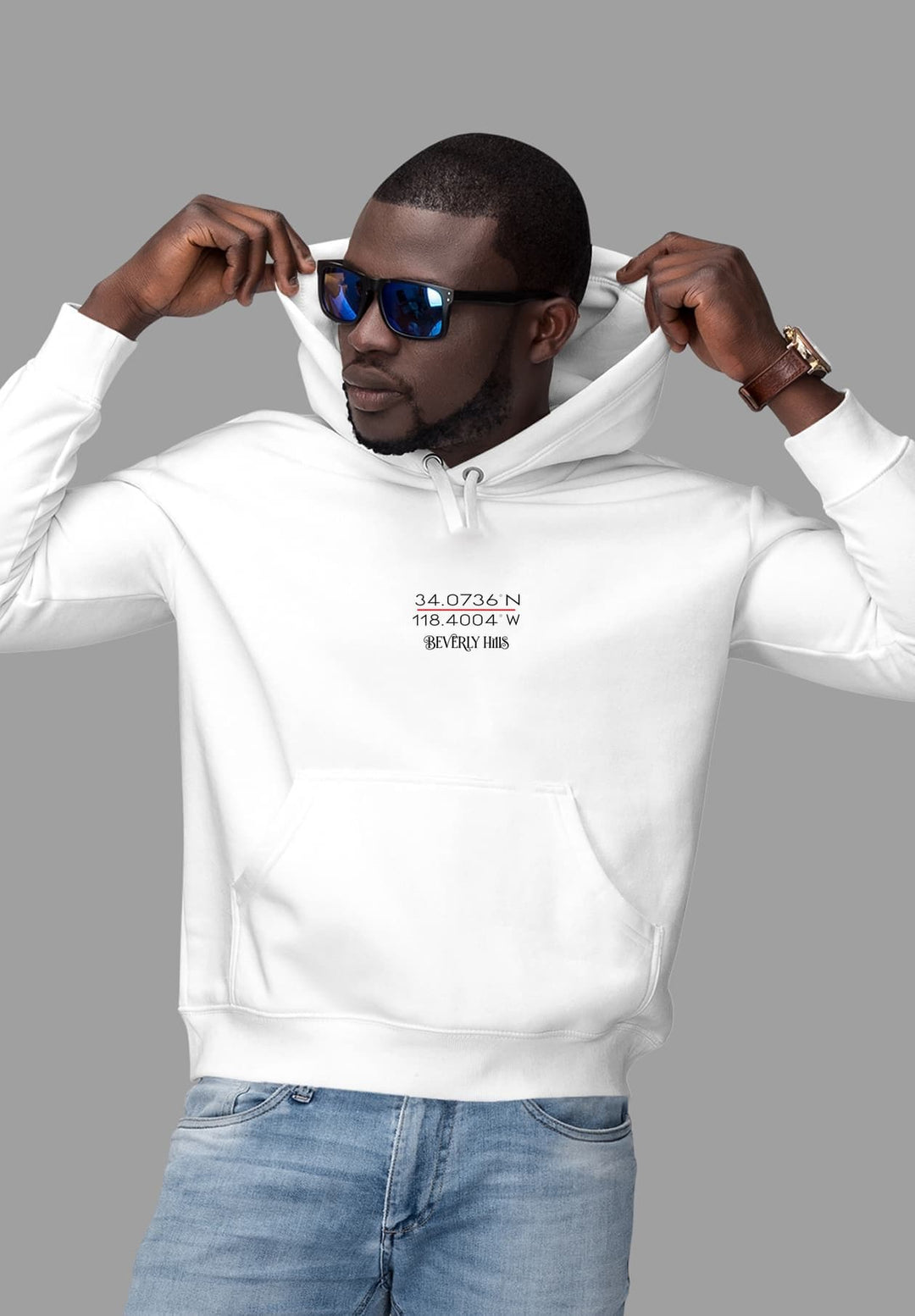 An individual displaying a white hooded sweatshirt adorned with the geographical coordinates of Beverly Hills in red and white.