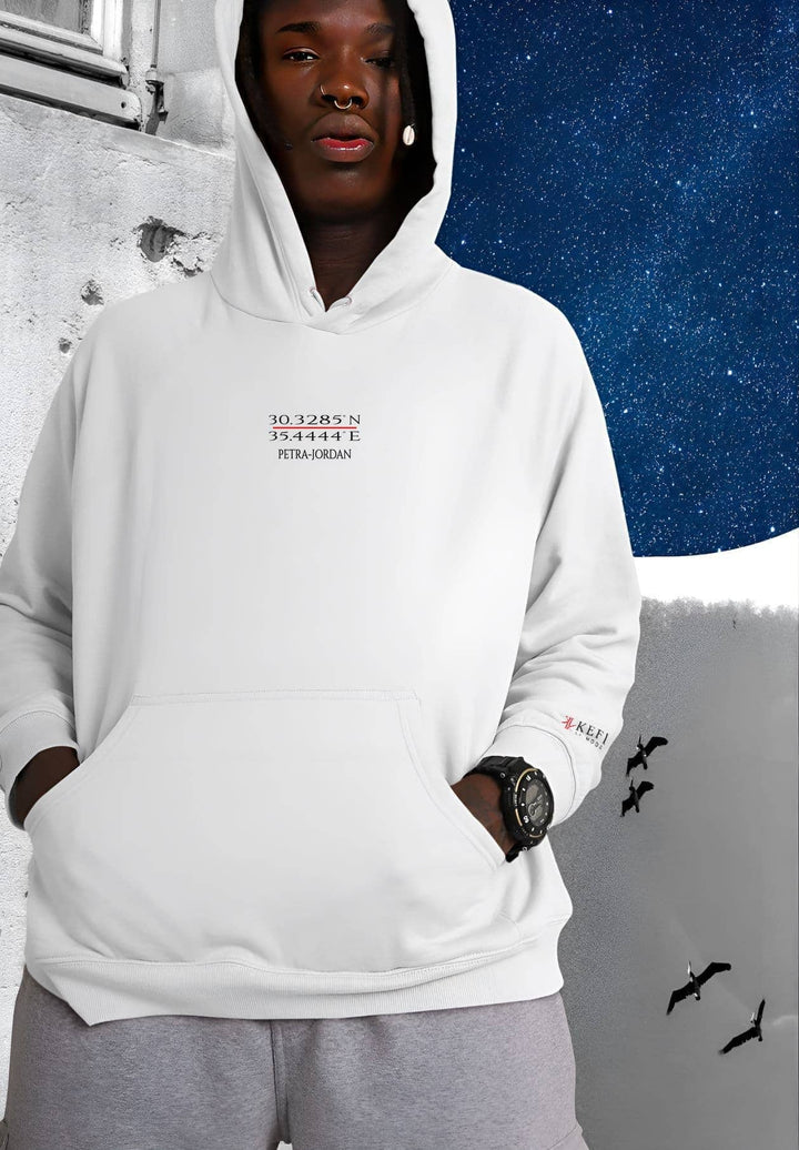 A man standing wearing a white Petra hoodie featuring the KEFI La Mode logo.