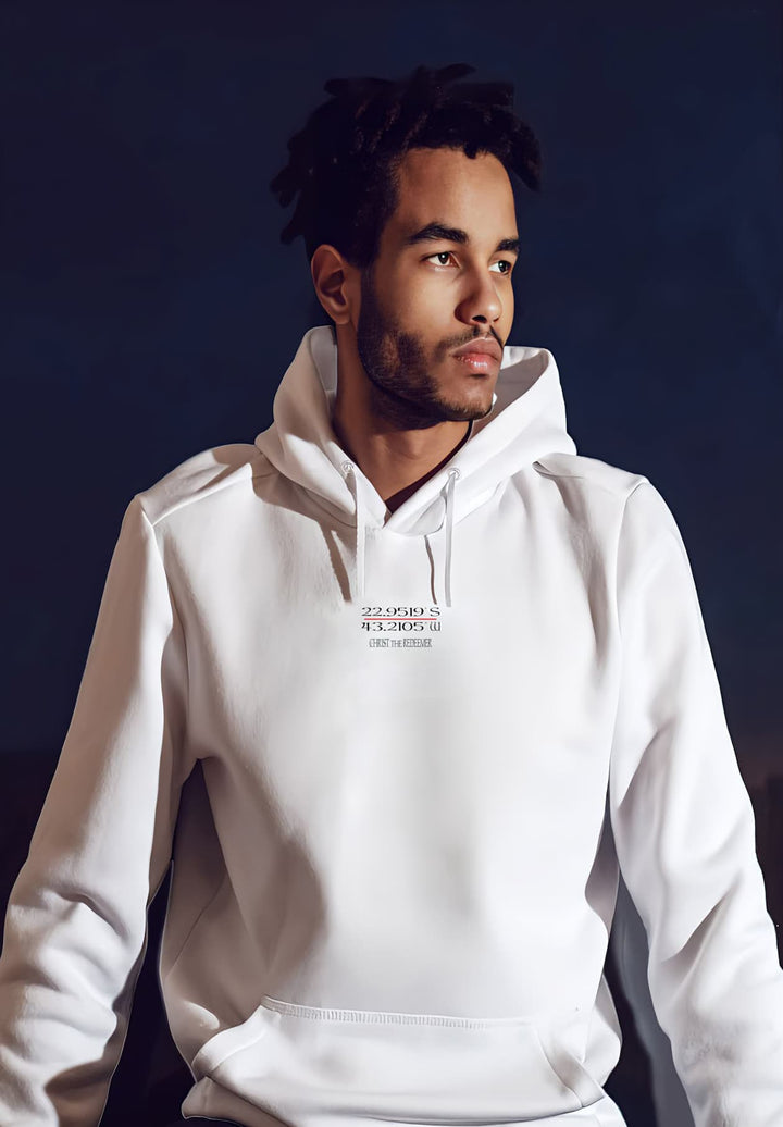 A gentleman with dreadlocks and a beard wearing a white hoodie while sitting looking in the distance.