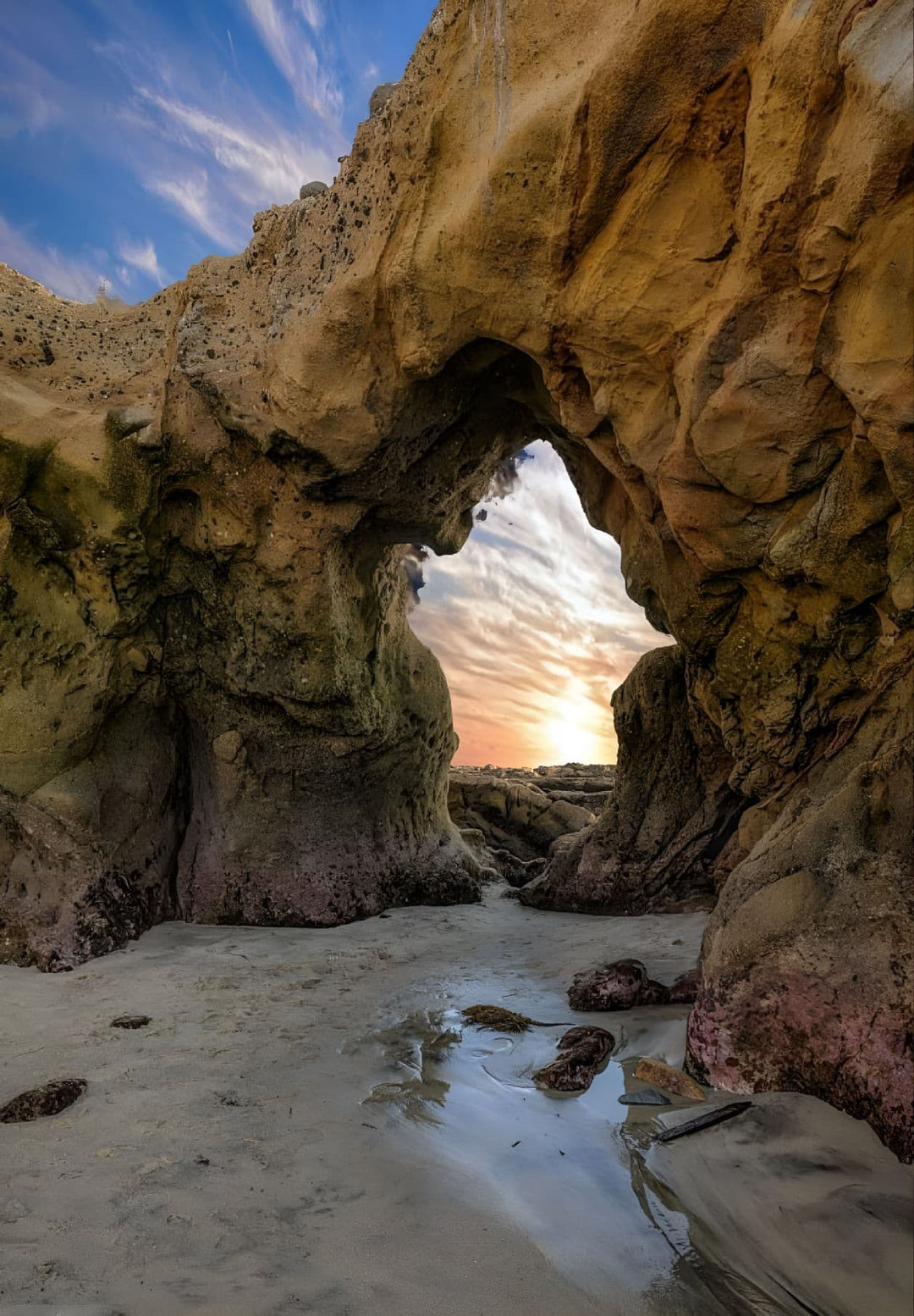 In Laguna Beach, California, the sun sets over the Pacific Ocean and streams through a natural ghost arch.