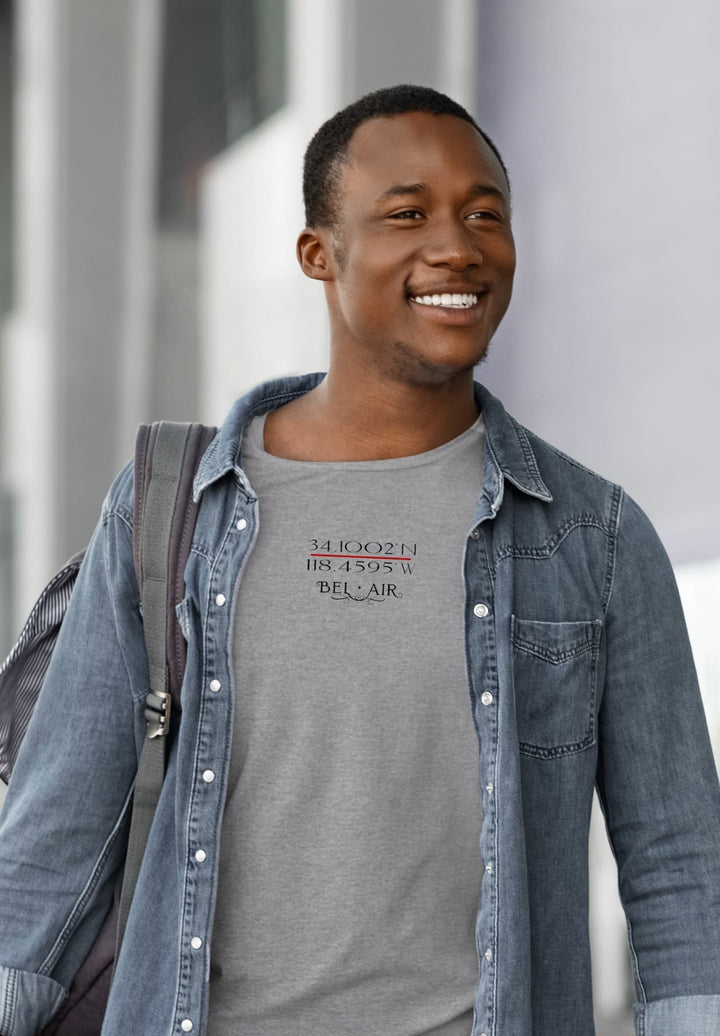 Wearing a relaxed gray tee and exuding an optimistic vibe in the sunshine, a man strolls outdoors, accompanied by a brilliant smile.