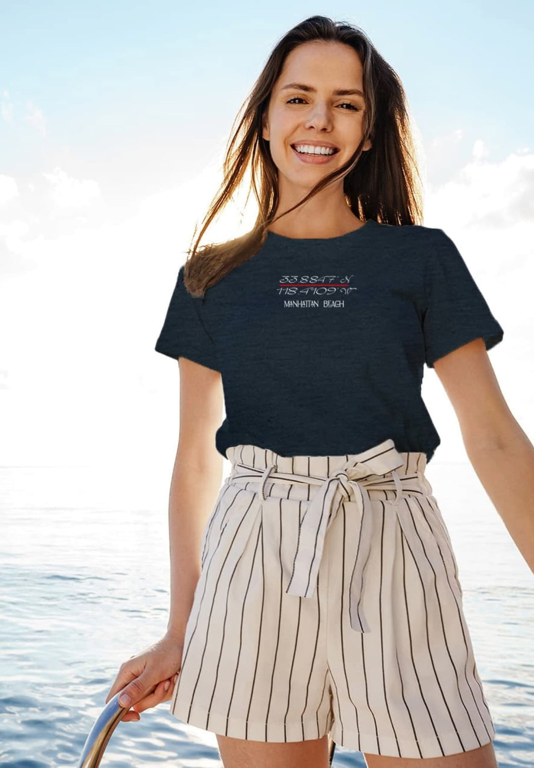Basking in the ocean breeze, a radiant woman aboard a yacht graces the moment with a warm smile, adorned in the vibrant charm of a soothing blue t-shirt.