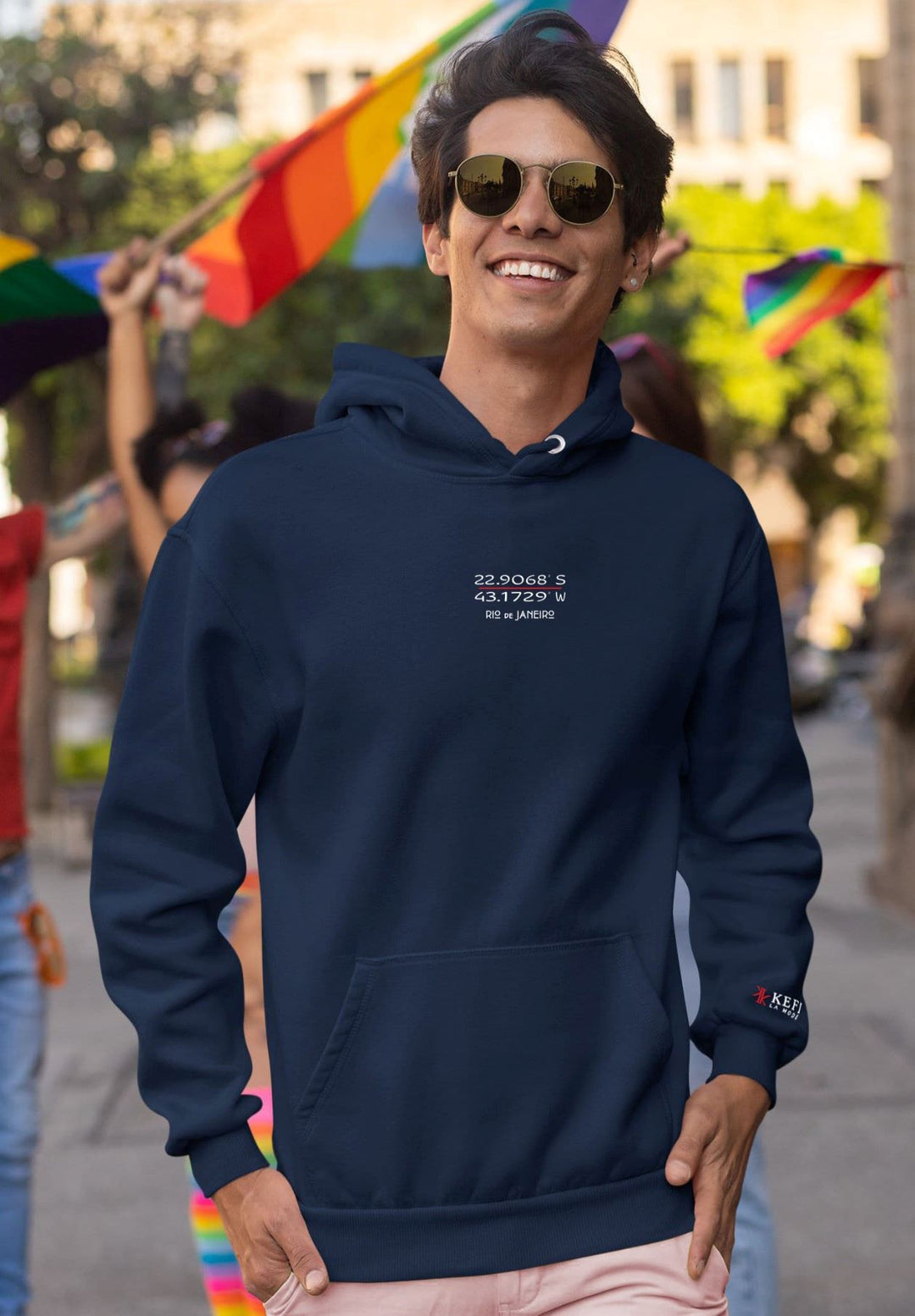 A gentleman attending the pride parade while displaying a blue hoodie with the city of Rio de Janeiro's GPS coordinates on it.