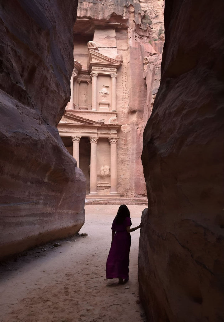A tourist is journeying via a steep passageway towards a stone mausoleum in Petra, Jordan.