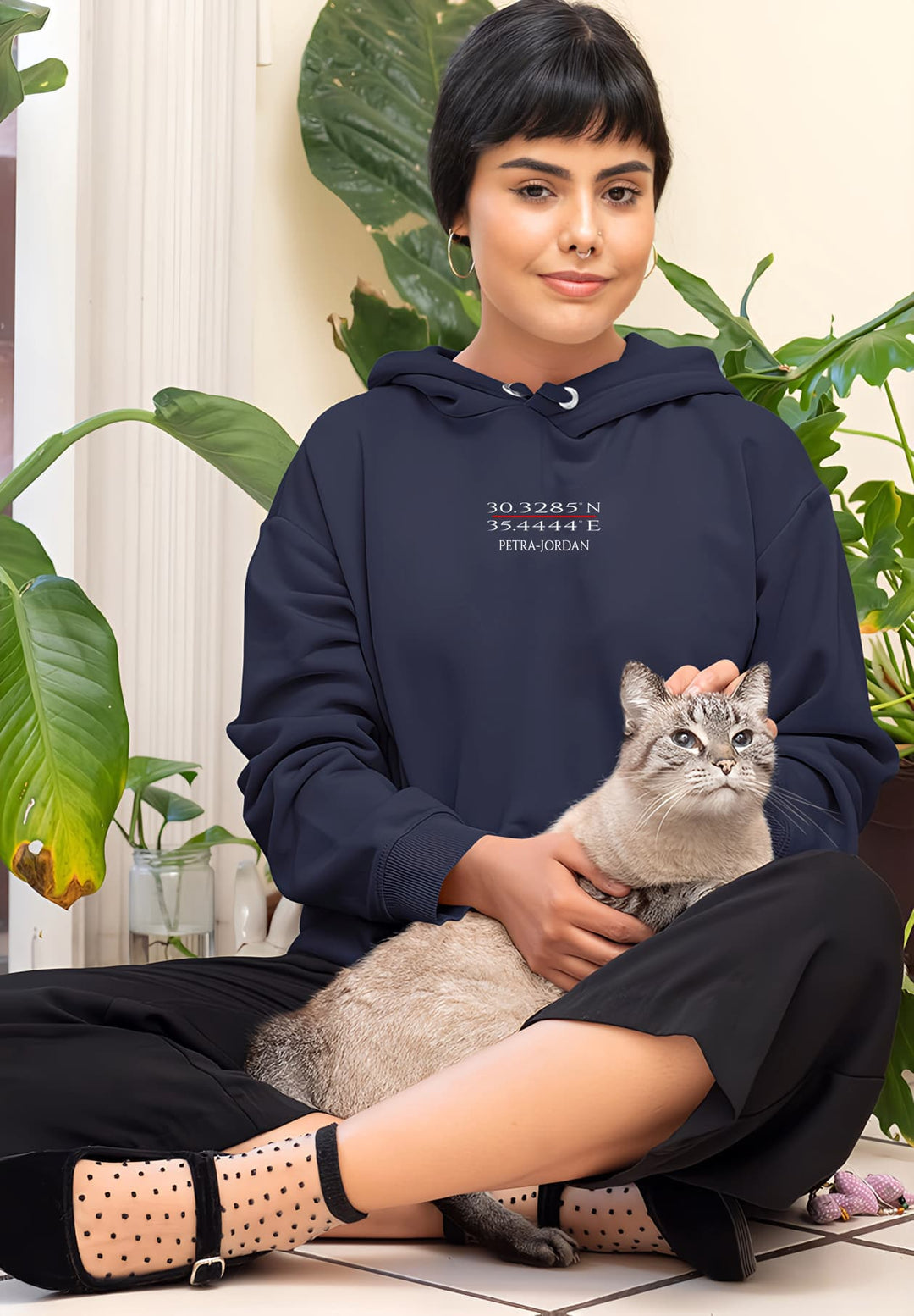 The woman's relaxed stance in the blue hoodie is beautifully accentuated by the gentle presence of the cat.