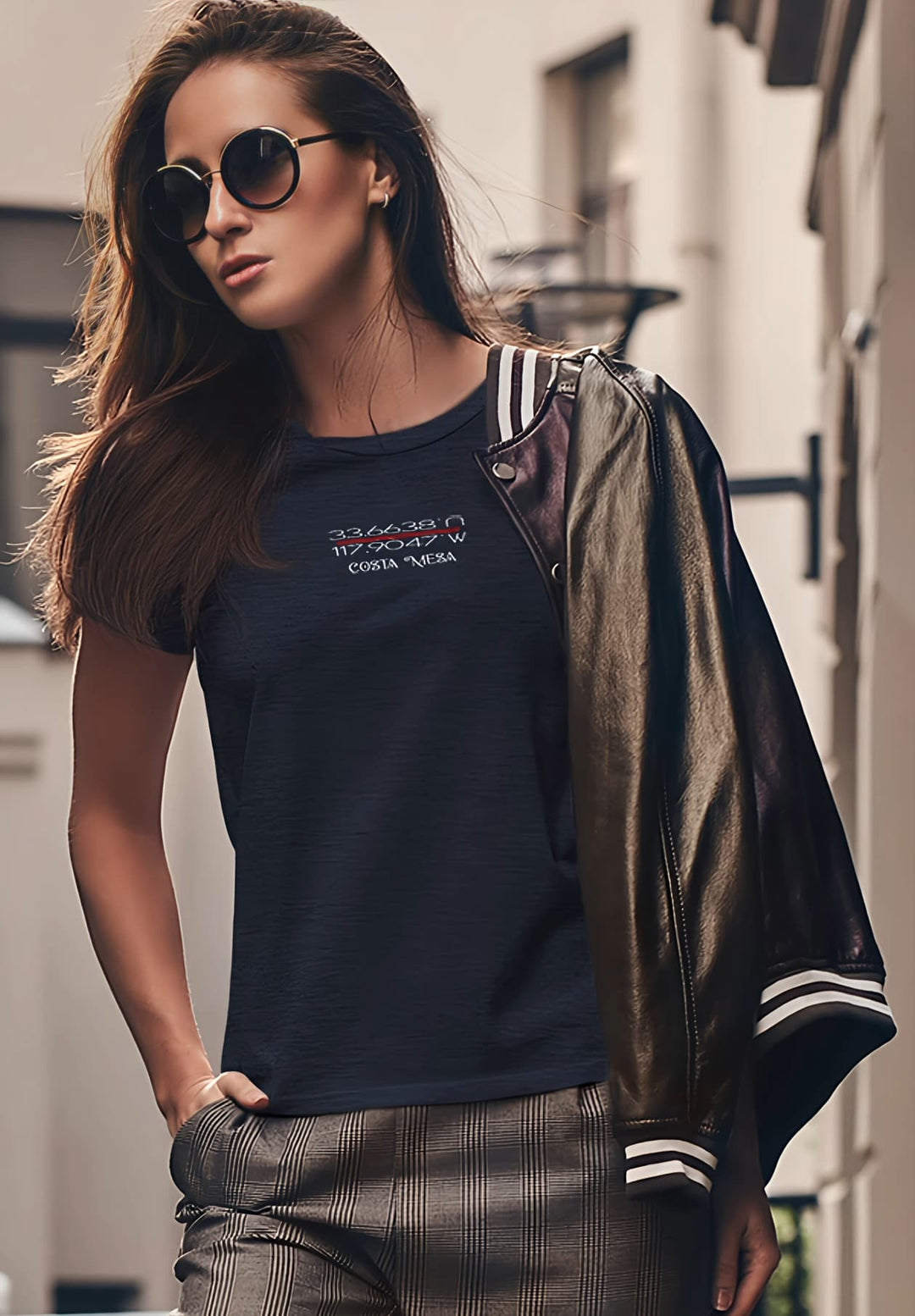 A woman wears a blue t-shirt, sunglasses, and a leather jacket creating a captivating blend of style that reflects both confidence and a touch of rebellious elegance.