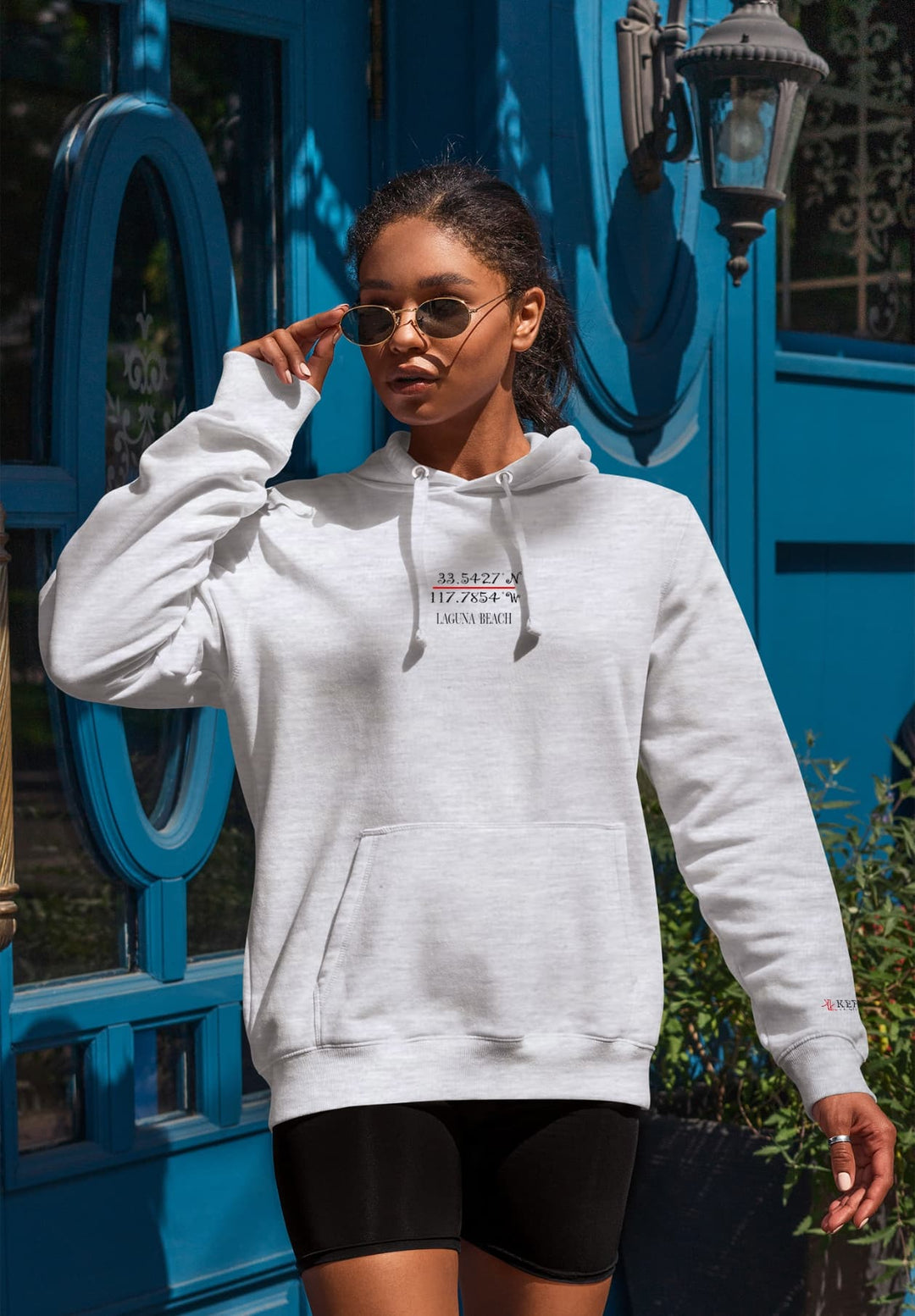 In front of the blue door, the woman in black shorts and a gray hoodie creates a striking image that combines urban chic with a touch of classic simplicity.