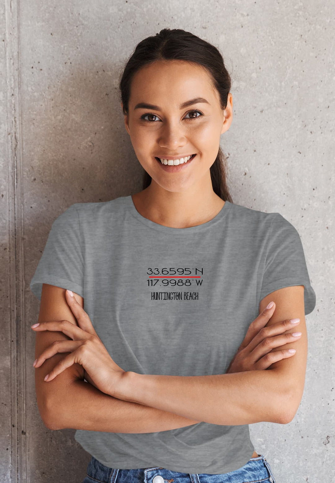 With an air of confidence and a touch fashion, the woman leans against the wall, arms crossed, wearing a stylish gray T-shirt that adds to her allure.