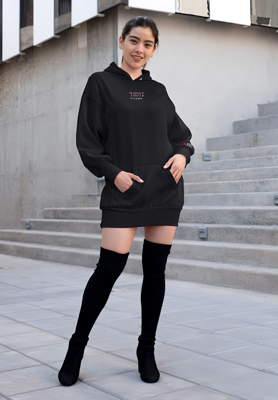 Striking a pose, the woman in a sleek black Paris hoodie and knee-high boots, commanding attention effortlessly.