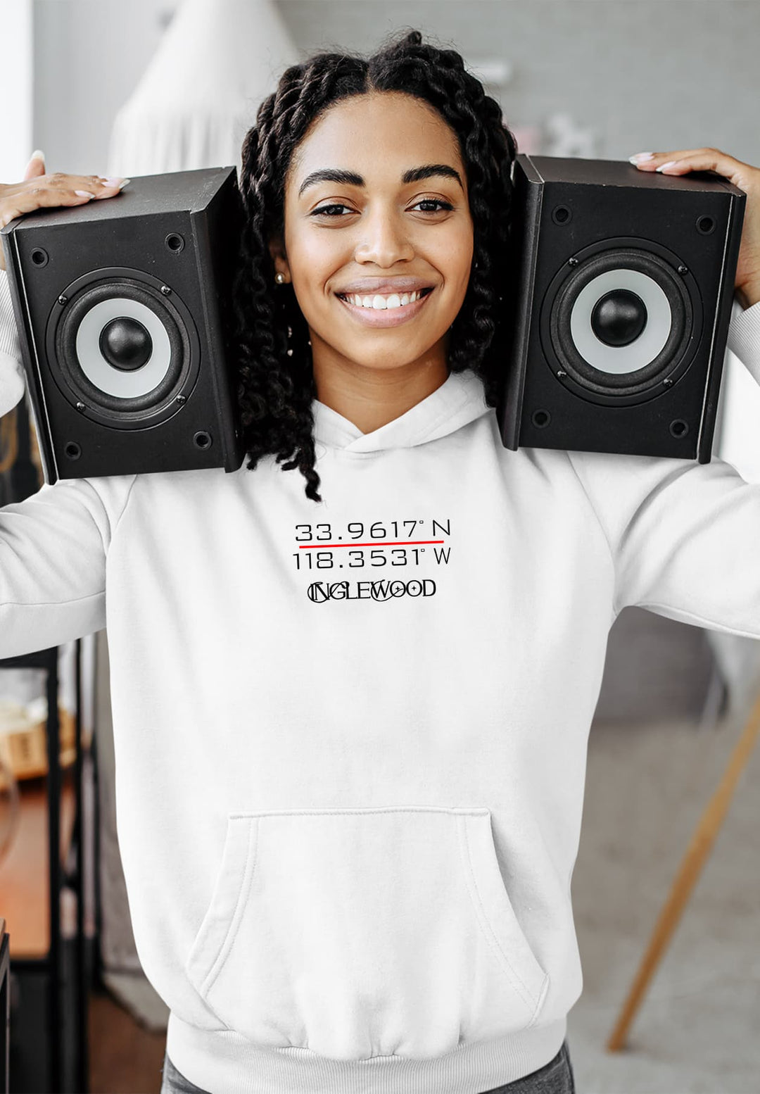 Standing with a smile, the woman in a white hoodie holds speakers close to her head, and creates a moment of musical joy.