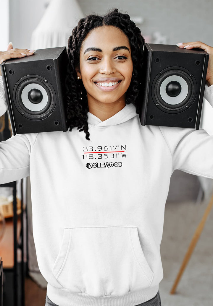Standing with a smile, the woman in a white hoodie holds speakers close to her head, and creates a moment of musical joy.