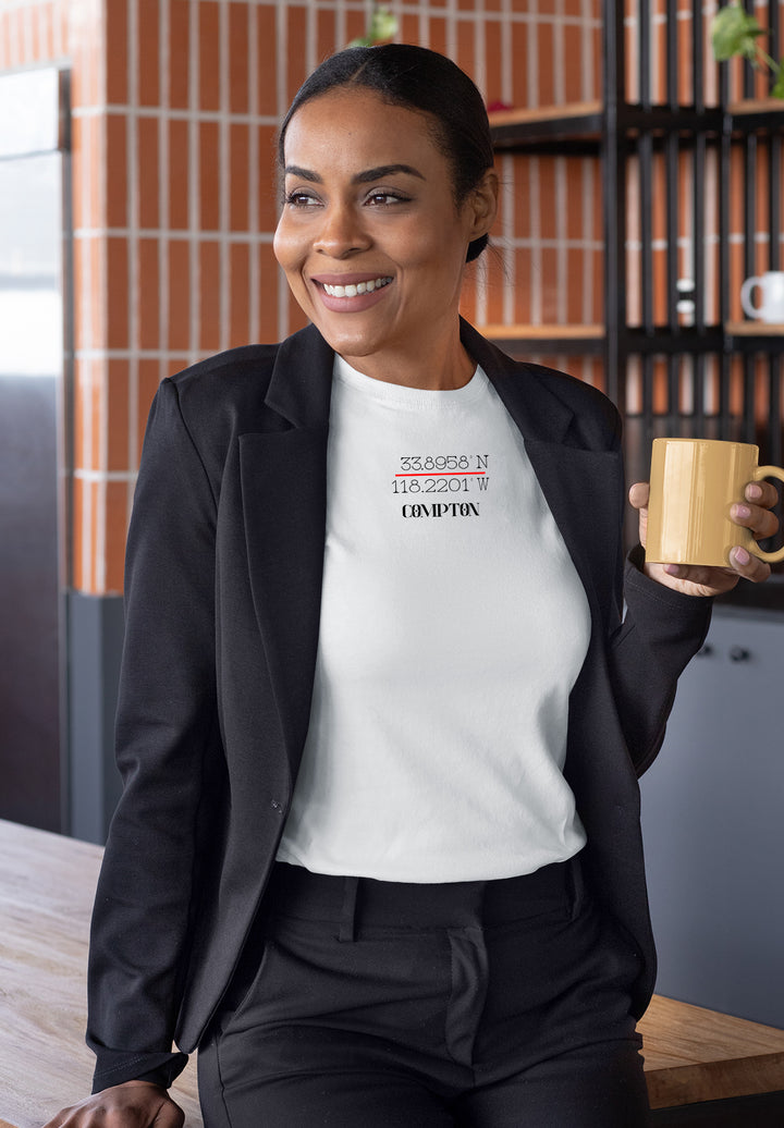 A warm, stylish woman in a white t-shirt and jacket holding a coffee cup, her smile reflecting a moment of simplicity in everyday life.