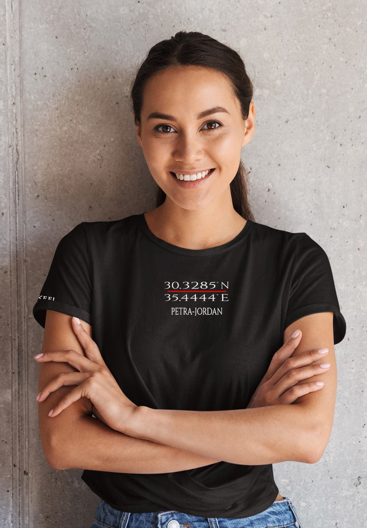 Radiating confidence and joy, a woman stands in a timeless ensemble – a black logo t-shirt and jeans, arms crossed, and a captivating smile.