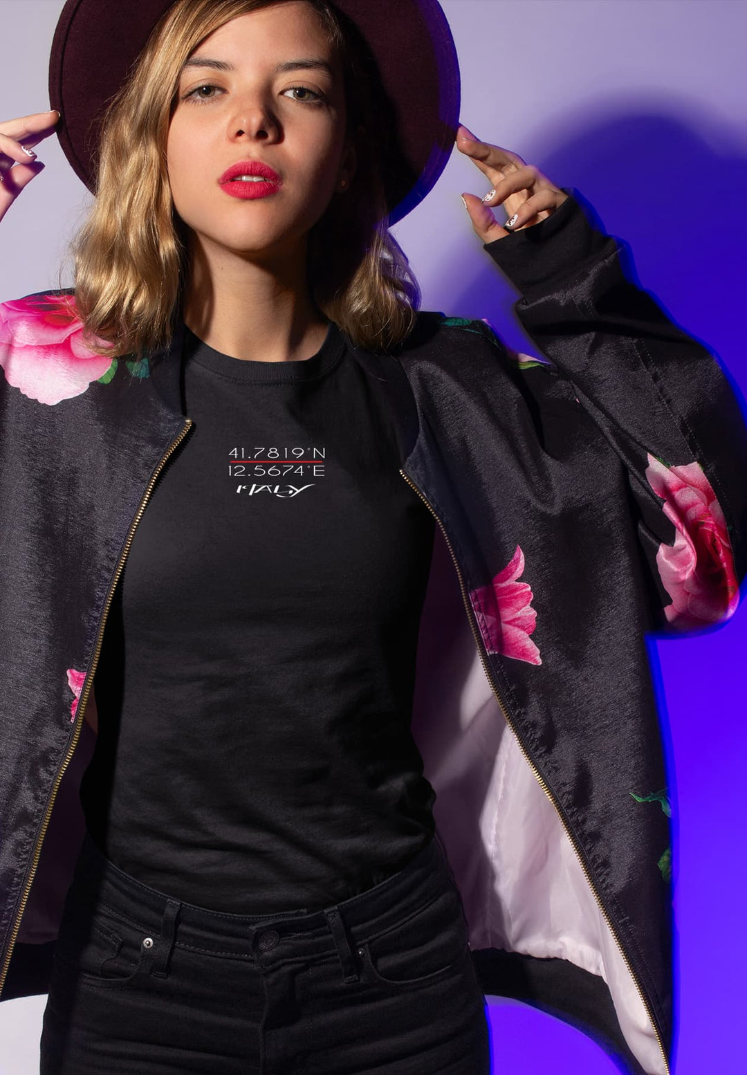 Exuding an air of cool sophistication, a woman stands confidently in a black t-shirt and jacket, adorned with a stylish hat that completes her chic ensemble.