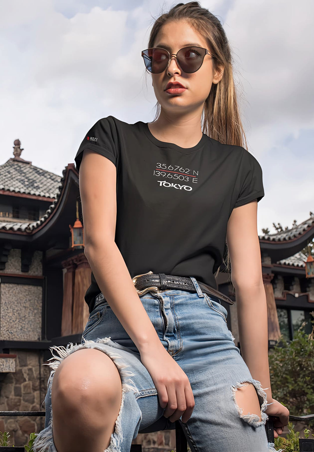 A woman stands by an oriental house, her black tee blending with the mystique, a moment painted with timeless beauty.