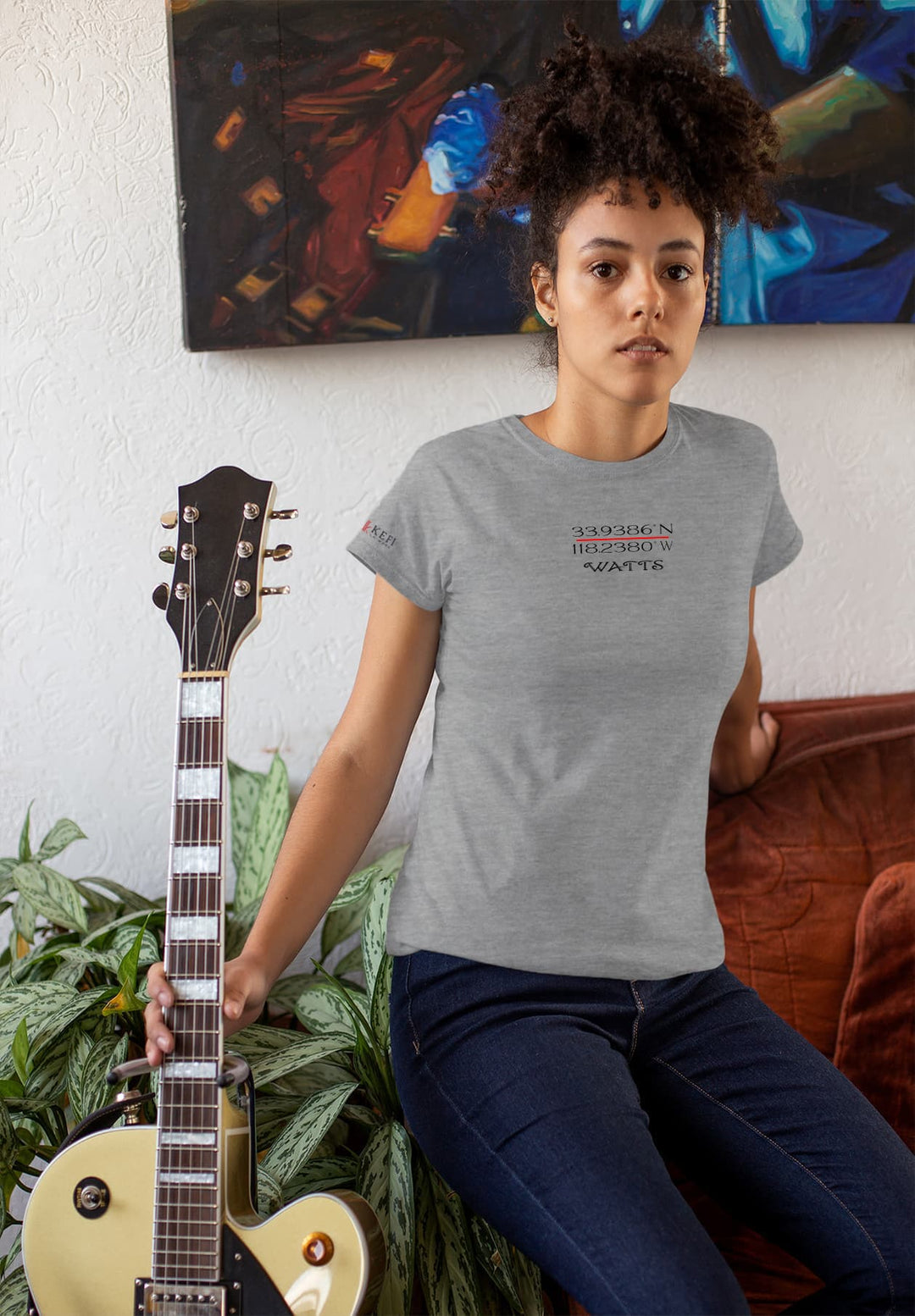  The young woman lounges casually beside a guitar on a couch, in a gray T-shirt, creating a scene of relaxed comfort.