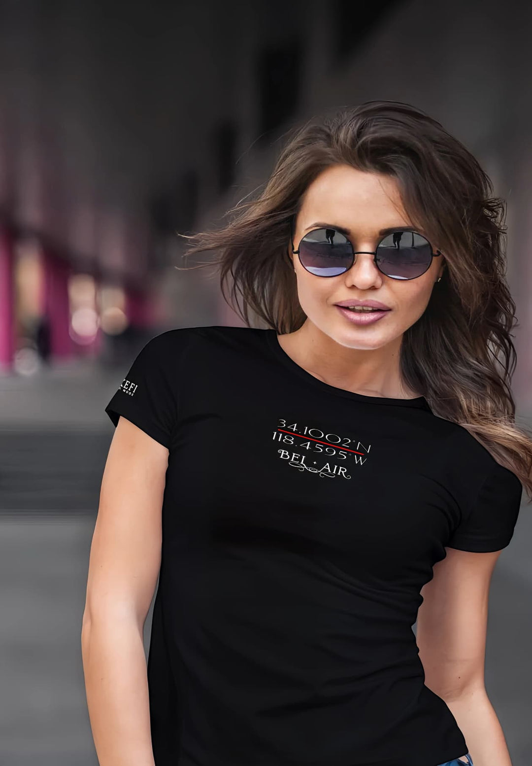 The woman wears sleek sunglasses and a black logo T-shirt with effortless coolness and a sense of confidence.