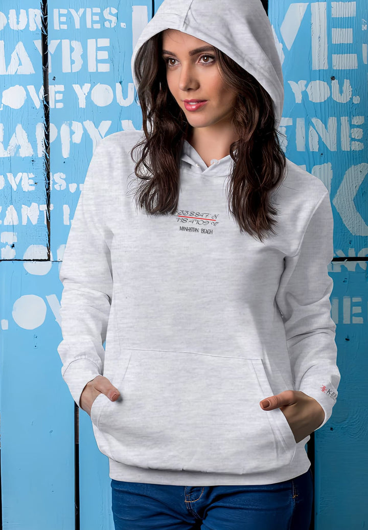 In front of the blue wall, the woman exudes a stylish aura, accentuated by the gray Manhattan Beach hoodie.