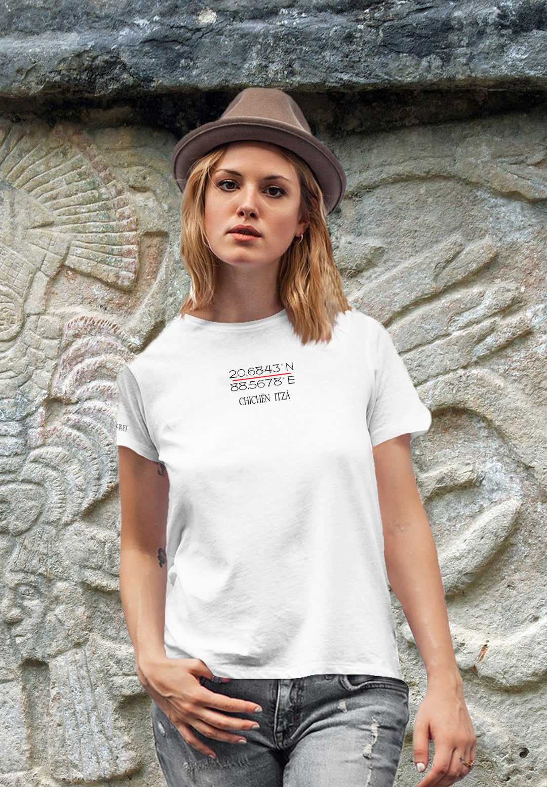 A woman wears a hat and white t-shirt on a rustic stone wall, combining modern style with the beauty of the past.